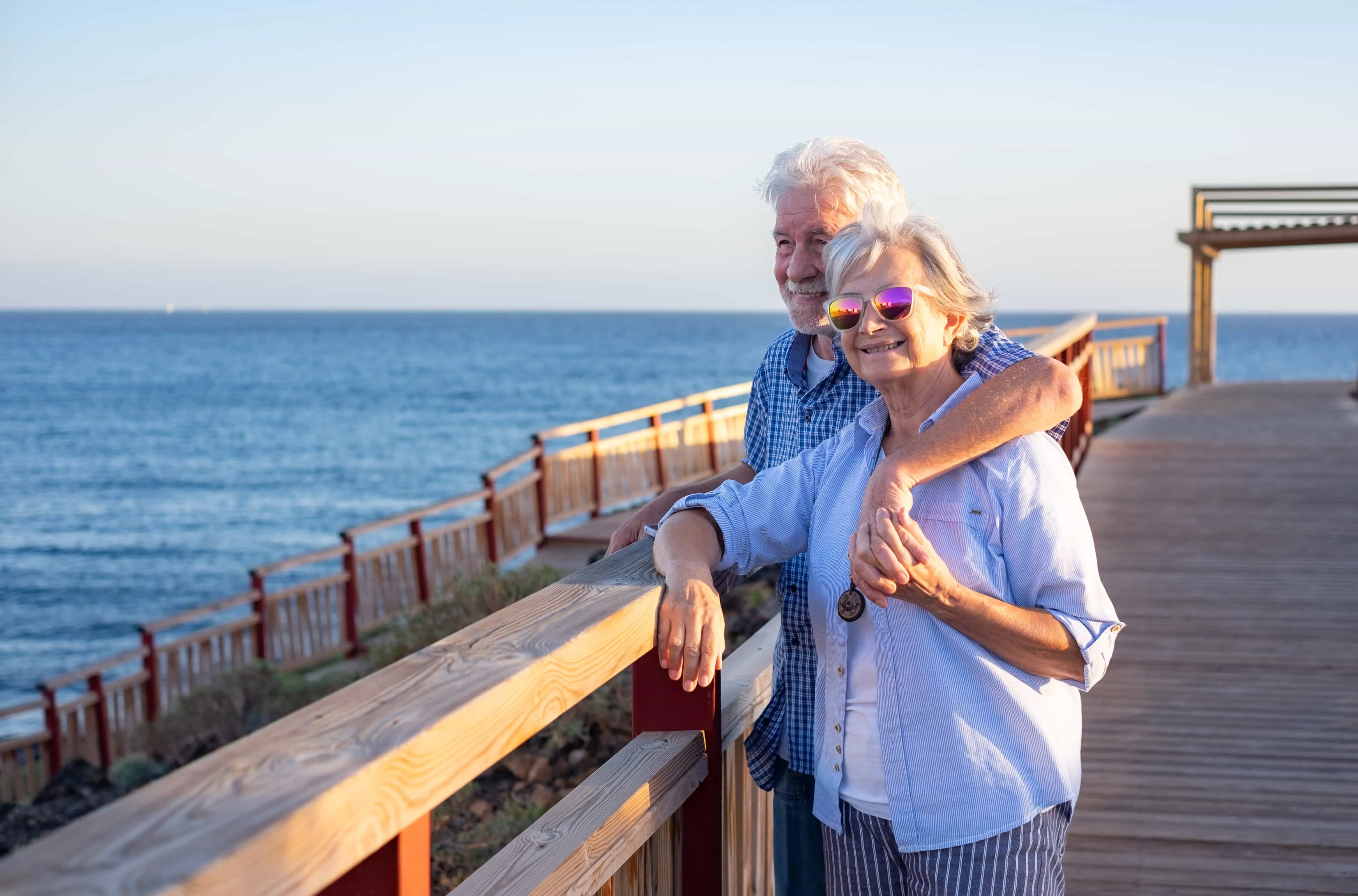Handsome relaxed senior couple of retirees hugging face the sea enjoying vacation and free time at sunset