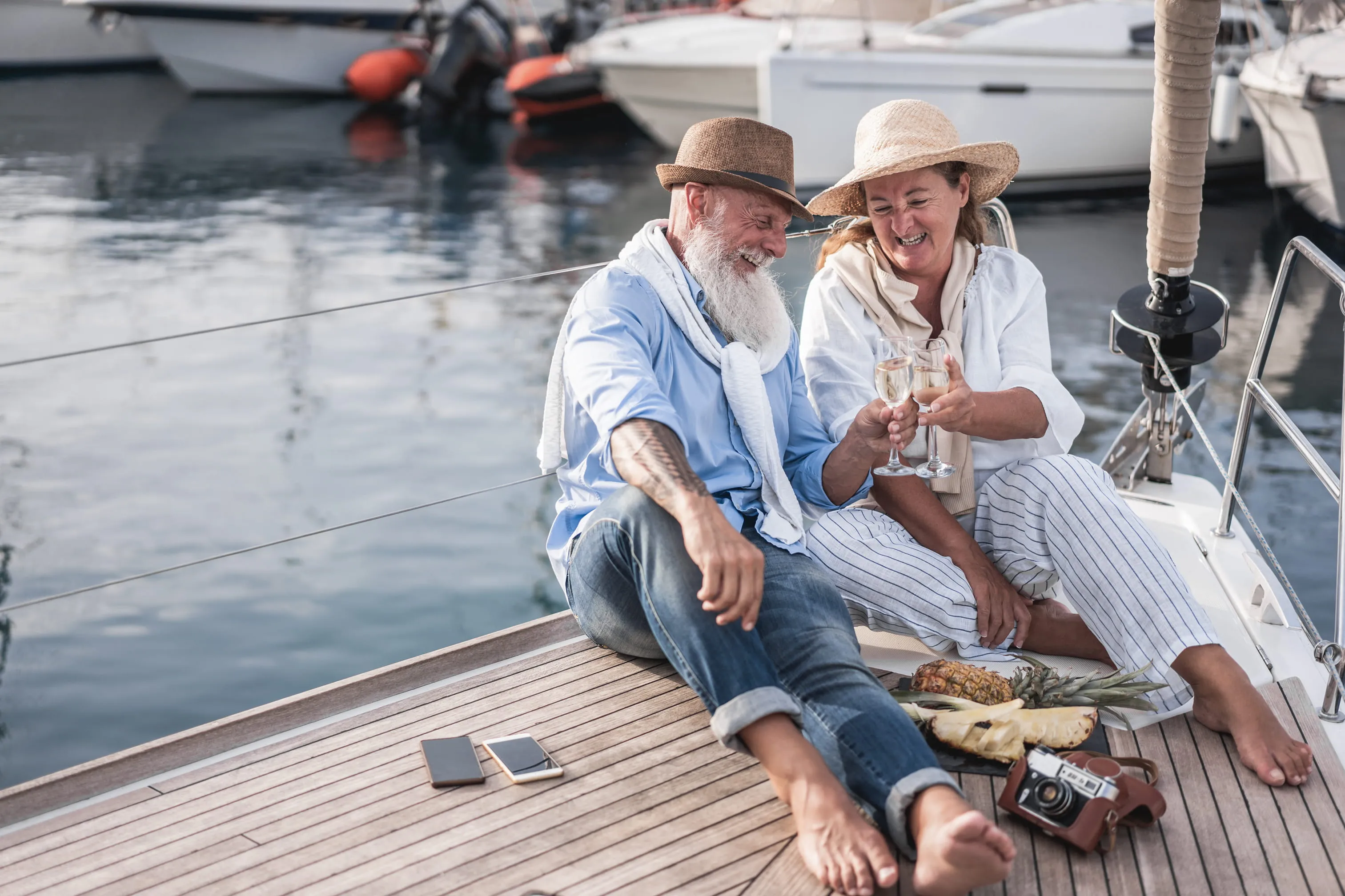 Senior couple cheering with champagne on sailboat during summer vacation